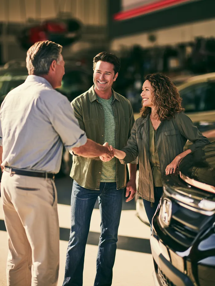 American couple shaking hands with a repair shop manager beside their finished car